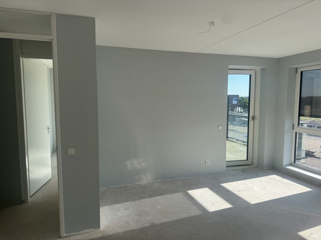 Lege kamer in een nieuw appartement met lichtgrijze wanden, een betonvloer en een deur naar het balkon