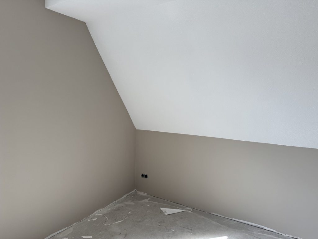 Zolderkamer in een nieuwbouwwoning met een schuine wand en strak afgewerkte muren in een zachte tint