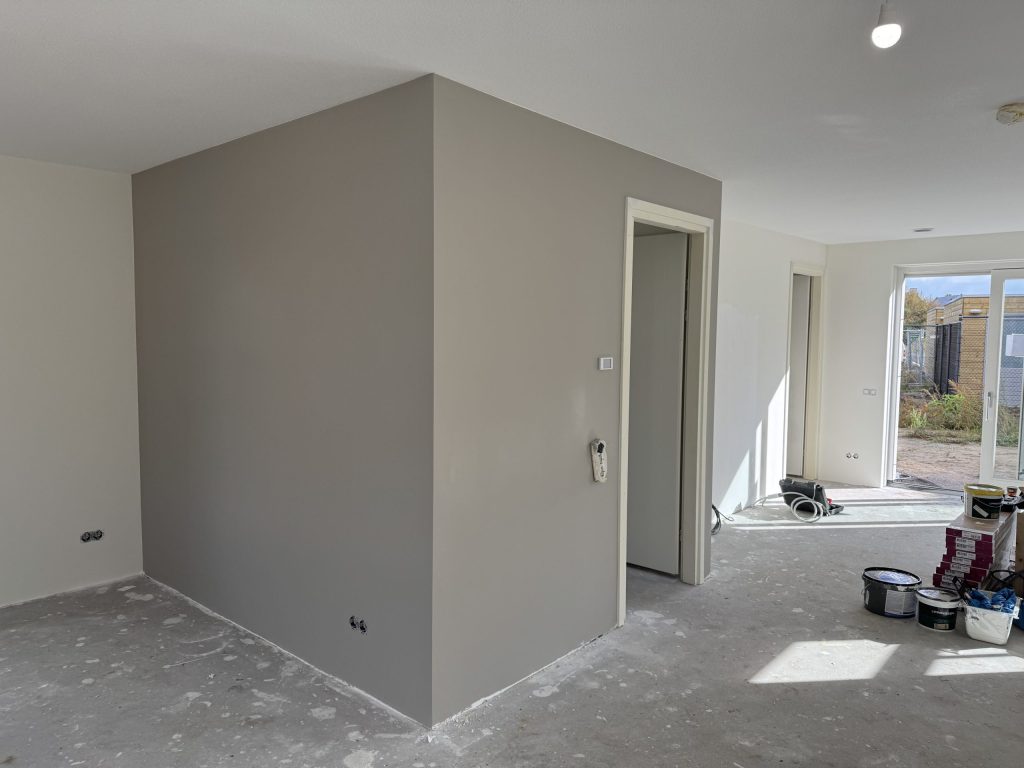 Nieuwbouwwoning met een pas afgewerkte grijze wand en verfemmers op de betonvloe