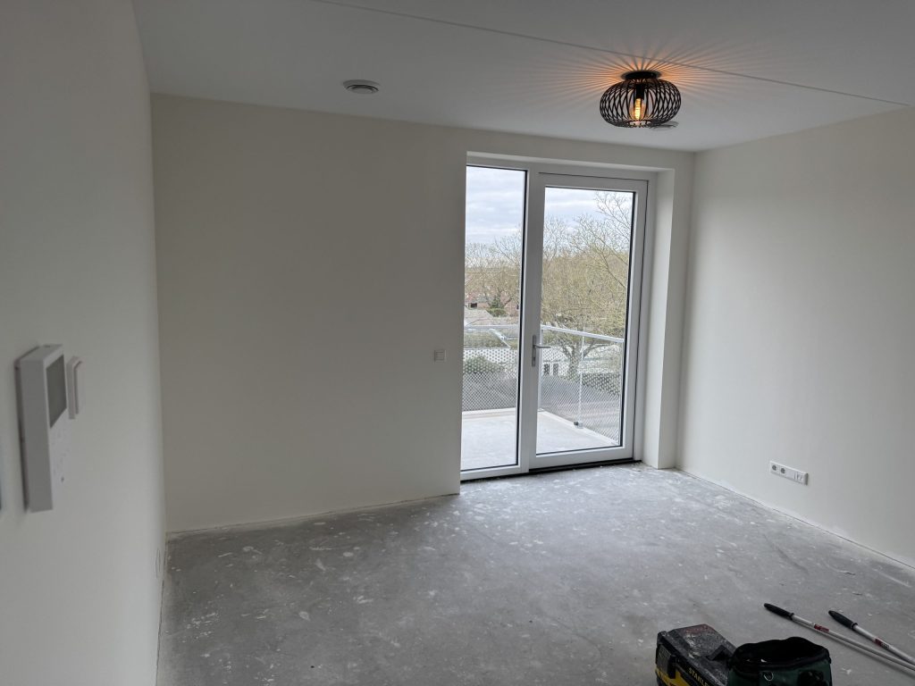 Kamer in een appartement op hoogte met witte wanden, een balkondeur en gereedschap van de behanger op de vloe